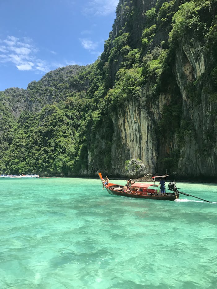 Scenic view of a traditional Thai longtail boat on emerald waters with lush limestone cliffs in Thailand.